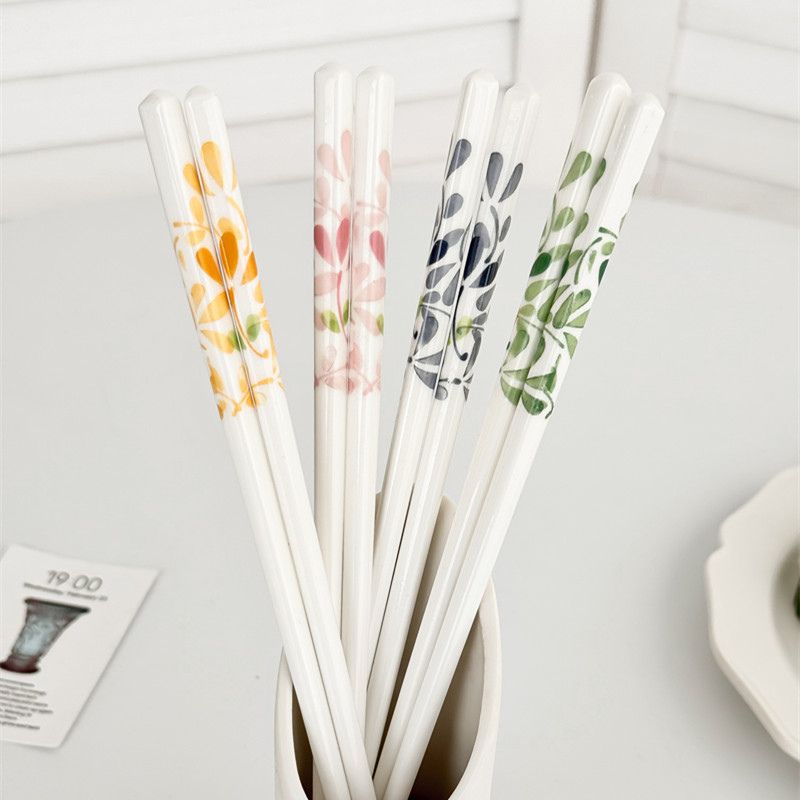 Baguettes en céramique aux motifs de feuilles gris, roses, orangés et verts, présentées dans un récipient blanc.