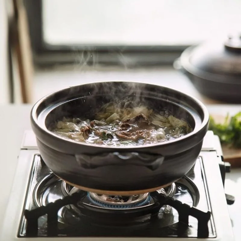 Marmite japonaise Donabe noire sur un réchaud à gaz, avec un bouillon fumant.