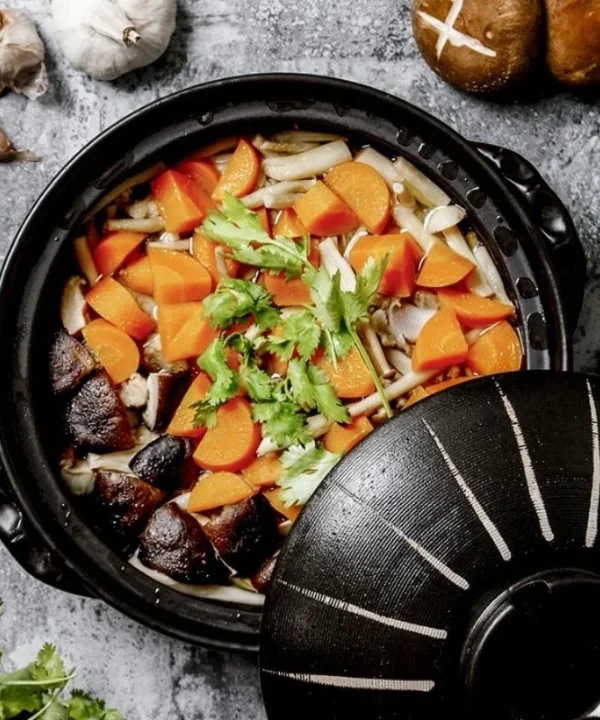 marmite-japonaise-donabe-noire-legumes-vue-dessus.webp Marmite Donabe noire garnie de légumes et de champignons, vue de dessus avec son couvercle décalé